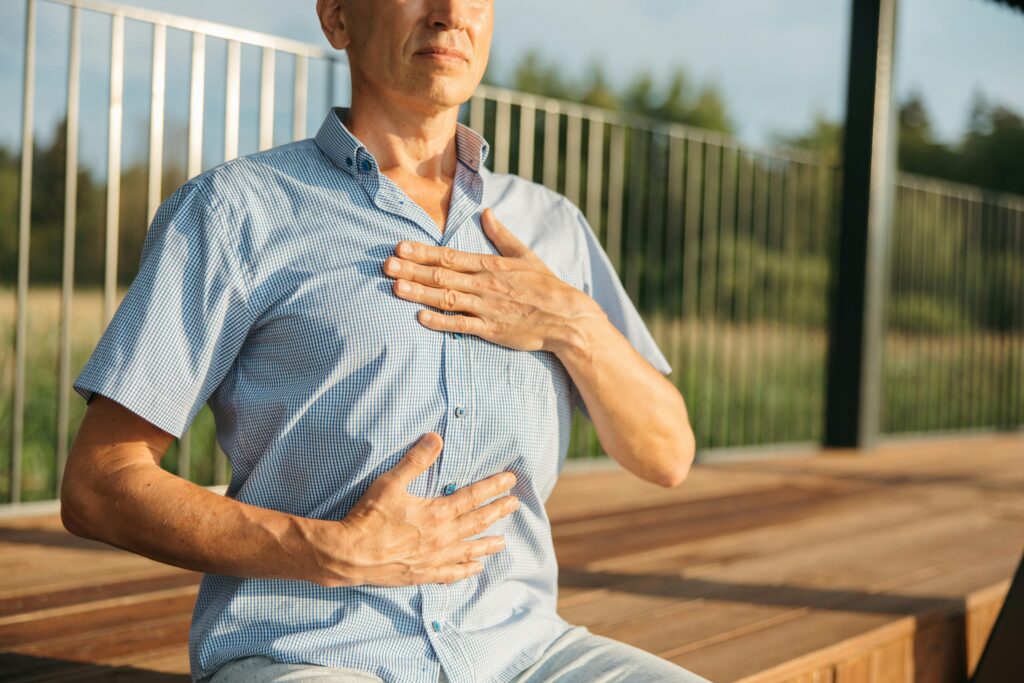 A man practicing relaxation with hands on chest and abdomen outdoors.